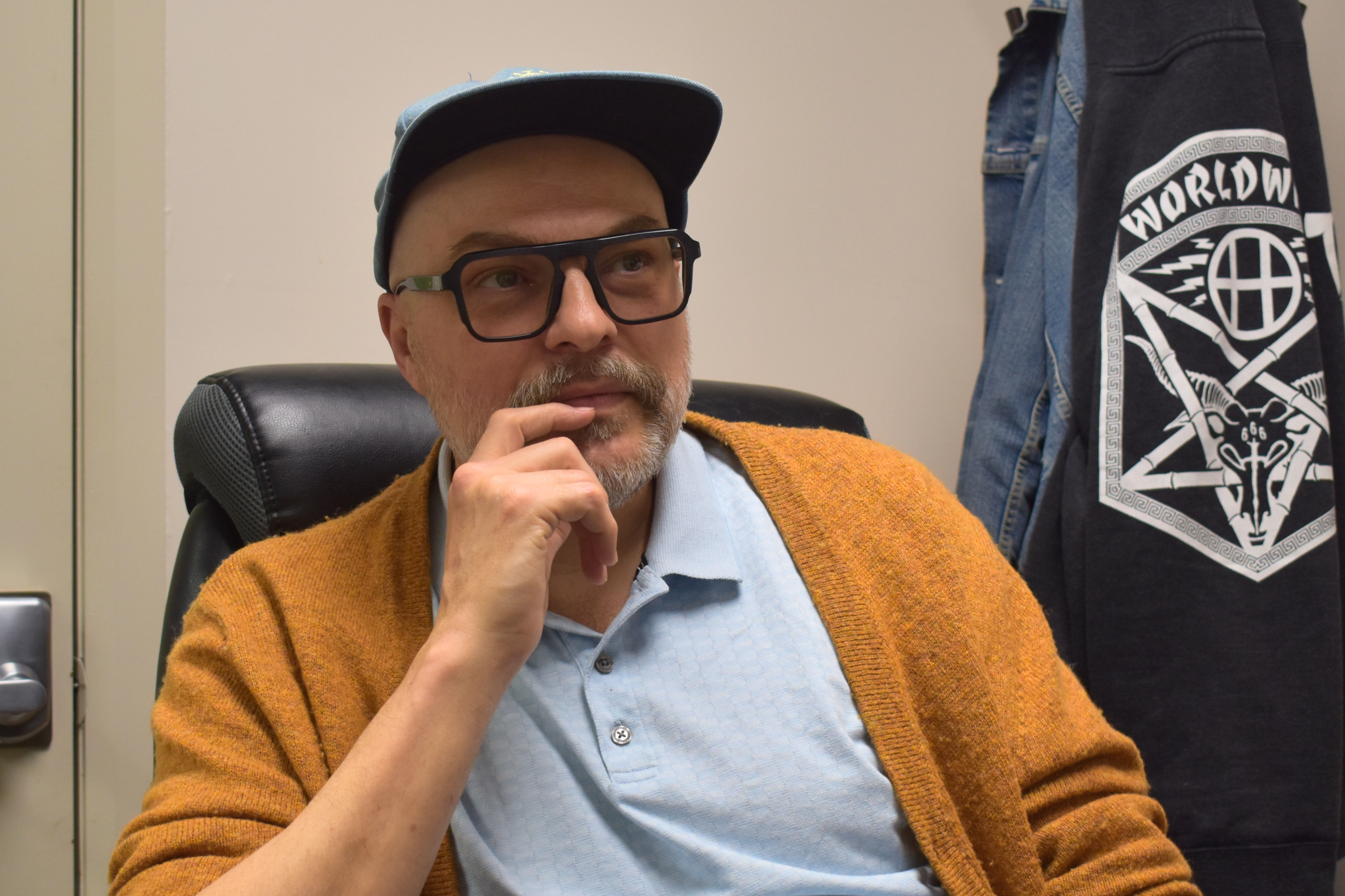 Photo of Chris Friesen, Manager of Collaborative Care at PARC, seated and looking directly at the camera with his hand resting near his chin. He is wearing glasses, a light blue polo shirt, and an orange cardigan.