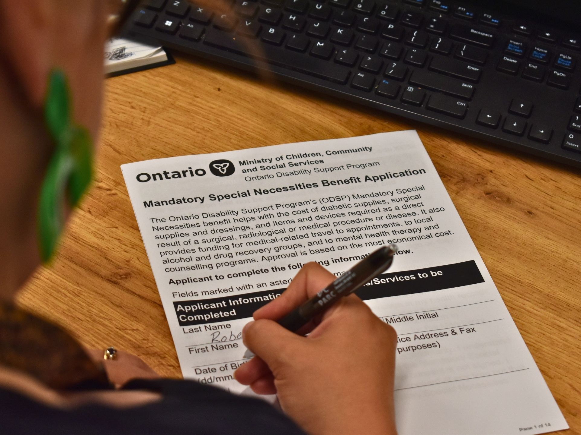 Close-up of a person filling out an Ontario Disability Support Program (ODSP) “Mandatory Special Necessities Benefit Application” form on a desk, with a keyboard nearby.